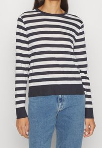 Langarm gestreiftes Oberteil in Marineblau und Elfenbein, mit Rundhalsausschnitt und lässigem Schnitt, kombiniert mit blauen Jeans.