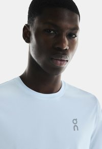 Lichtblauw sport T-shirt van een textuurmateriaal, met een ronde hals en een grijs logo op de voorkant.