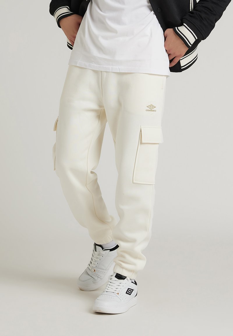 Pantaloni cargo bianchi realizzati in materiale morbido, con due tasche laterali, polsini elasticizzati e un piccolo logo in rilievo. Abbinati a sneakers bianche.