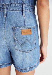 Jasnoniebieskie szorty dżinsowe o klasycznym kroju. Posiadają tylną kieszeń z brązową skórzaną metką z wyhaftowanym logo "Wrangler".