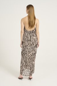 Rochie maxi din material transparent, cu imprimeu zebra în nuanțe de maro și crem, având spatele decupat și talie strânsă. Modelul poartă sandale cu vârful descoperit.