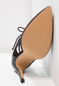 Chaussure à talon haut noire avec un motif texturé reptile, bout pointu et talon aiguille fin. Semelle de couleur claire avec texture nervurée.