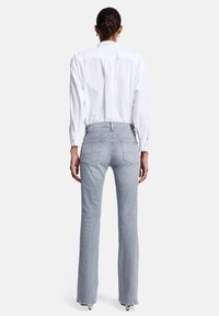 Lichtblauwe, uitlopende spijkerbroek met een middelhoog taille, twee achterzakken en een subtiel stikselpatroon. Draagt bij een fris wit overhemd.