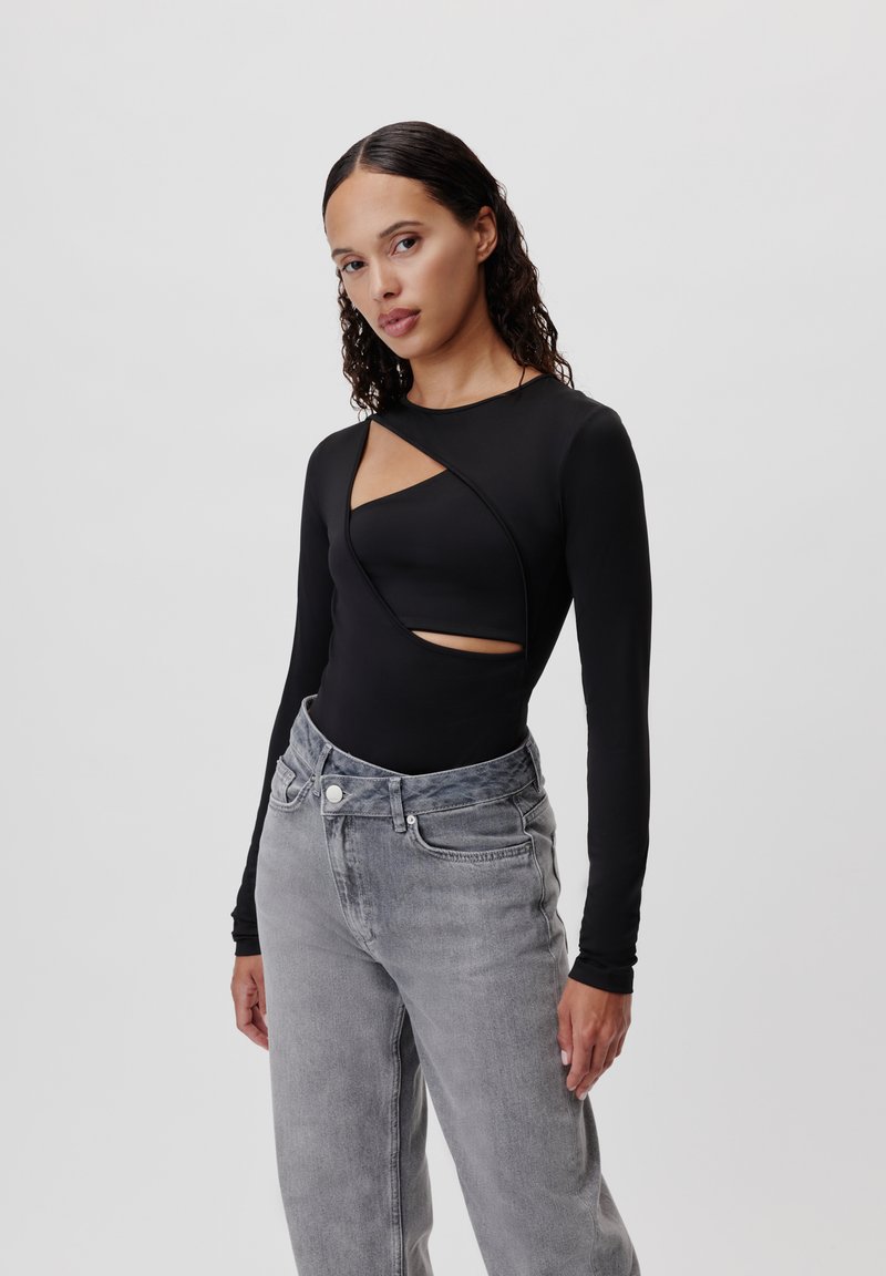 Body lungo nero con design a tagli e texture liscia, abbinato a jeans grigi sbiaditi a vita alta.