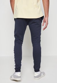 Tengerészkék pamut keverék jogger nadrág, slim fit fazon, bordázott szegélyekkel és kontrasztos fehér logónyomattal a bal lábszáron. Könnyű és kényelmes kialakítás.