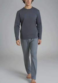 Maglietta grigia a maniche lunghe abbinata a pantaloni a righe blu chiaro. La maglietta ha un collo rotondo; i pantaloni presentano righe verticali e una vestibilità rilassata.