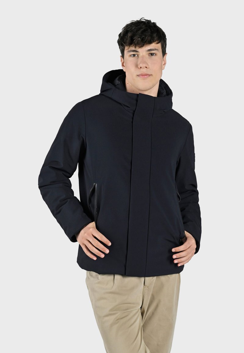 Giacca isolante blu navy con colletto alto e cappuccio, dotata di tasche laterali con zip e una texture liscia e opaca.