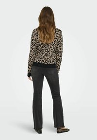 Pull en imprimé léopard beige et noir, design ajusté, bord-côtes au bas et aux poignets, associé à un jean noir évasé foncé et des ballerines noires cloutées.