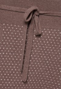 Tissu tricoté marron avec un motif texturé de petits cœurs blancs. Présente une taille côtelée avec un détail de cordon de serrage noué.