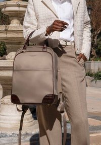 Sac à dos beige avec des accents en cuir texturé, deux poignées et des bretelles réglables, présentant une finition lisse et un design minimaliste.
