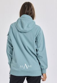 Giacca con cappuccio in tessuto azzurro chiaro, con un logo "SLADE" sul retro, dettagli con zip sulle maniche e una vestibilità comoda con polsini a costine.