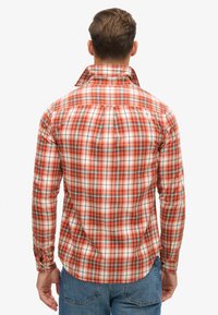 Camicia a quadri rossa e bianca con accenti blu, caratterizzata da collo alto e polsini con bottoni. Realizzata in tessuto di cotone leggero.