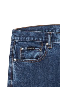 Džínsy z denimu v tmavomodrej farbe, s kontrastným oranžovým stehom, malou prednou vreckom a značkovou nášivkou na zadnom vrecku.