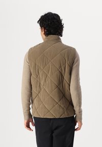 Gemusterte olivgrüne Weste mit hohem Kragen und strukturiertem Stoff, getragen über einem beigen Pullover, mit gerippten Bündchen und lässiger Passform.