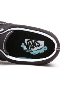 Fekete Vans cipő belső része fehér varrással, ComfyCush logo türkis színben fekete pöttyös háttér előtt. Lekerekített élek és sima felület.