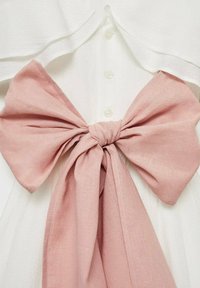Weißes Kleid mit durchgehendem Knopfverschluss und einer großen rosa Stoffschleife, die in der Taille gebunden ist, wodurch eine geschichtete Textur und eine markante Silhouette entsteht.