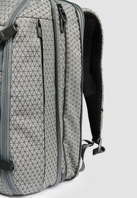 Zaino grigio con motivo a diamante, dotato di due scomparti con cerniera e spallacci imbottiti in rete per il comfort. Tessuto resistente e design elegante.