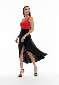 Top roșu fără mâneci, asortat cu o fustă maxi fluidă și neagră, cu o despicătură pe lateral, completat de sandale negre cu toc înalt și curele.