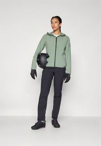 Grüne leichte Jacke mit Kapuze, schwarze Hose, schwarze Handschuhe und schwarzer Helm. Schuhe sind schwarz mit violetten Akzenten. Minimalistisches Design.