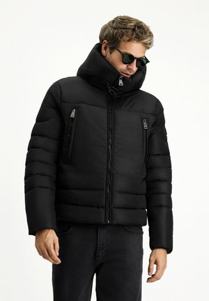 Chaqueta de plumas negra con un cuello alto, cierre de cremallera en la parte frontal y dos bolsillos en el pecho con cremallera. Presenta secciones acolchonadas y una textura suave.