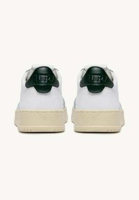 Hvide sneakers med en glat læderoverdel, grøn læderhælflap og tekstureret beige gummisål, som har diskret branding bagpå.