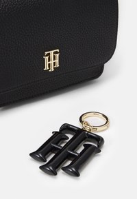 Czarna torba z teksturowanej skóry z złotym logo; wyposażona w czarny breloczek w kształcie litery na złotym pierścieniu, prezentująca elegancki design.