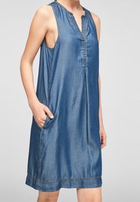 Džínová šaty bez rukávů s výstřihem do V, bočními kapsami a mírně rozšířeným siluetou. Disponují kontrastním šitím a volným, ležérním střihem.