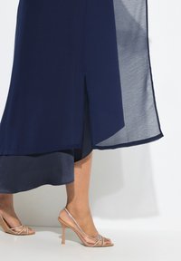 Marineblauwe gelaagde jurk met een zijsplit, voorzien van een lichtgewicht, doorzichtig overlay. Gepaard met naakte hoge hakken met delicate bandjes.