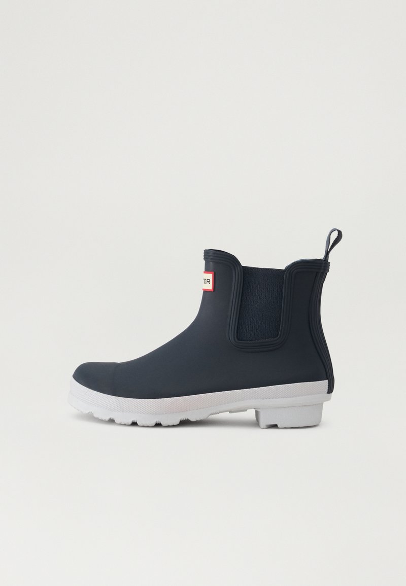Bota de tobillo de goma en color navy con paneles laterales elásticos, suela blanca, pestaña en el talón y suela texturizada para mayor agarre.