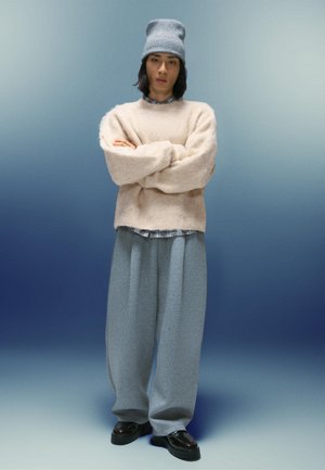 Jasnofioletowy, puszysty sweter, szare, oversize'owe dresy, czarne buty oraz jasnoniebieska, dziana czapka z teksturowanym wzorem, na tle gradientu.