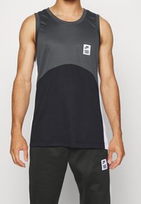 Débardeur de sport sans manches en noir et gris avec un col rond, présentant un patch logo et un design en color-block. Fabriqué en tissu lisse.