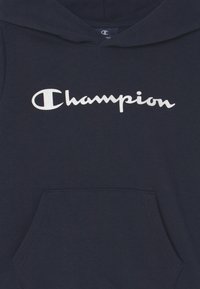Felpa blu navy realizzata in un morbido tessuto, con un grande logo bianco "Champion" sul petto e una tasca anteriore a marsupio.