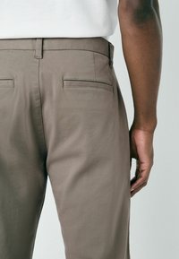 Brown chinos featuring a smooth, textured fabric, standard fit, and double back pockets with subtle stitching details.