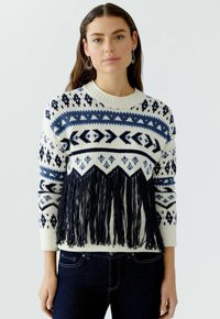 Gebreide trui met een witte basis, blauwe geometrische patronen en marineblauwe franjes aan de onderkant. Heeft een ronde halslijn en lange mouwen.