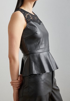 Vrouw draagt een mouwloze zwarte leren peplum top met kanten details bij de halslijn, gecombineerd met zwarte leren broek.