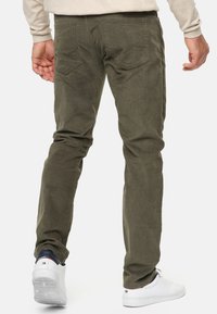 Oliven grøn kordfløjlsbukser med en slim fit, der har baglommer og en struktureret overflade. Båret med hvide sneakers.
