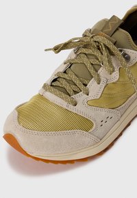 Beige and olive green sneaker featuring a mix of suede and mesh materials, textured laces, and a rubber sole with orange accent.