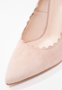Escarpin à bout pointu en suède beige doux avec des découpes festonnées le long du col et une doublure intérieure lisse. Semelle couleur beige clair.