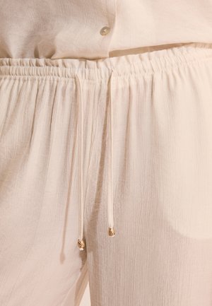 Hellbeige, locker sitzende Hose mit elastischem Bund und Kordelzug mit goldfarbenen Metallenden, kombiniert mit einem passenden Hemd mit Knöpfen.