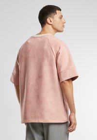 Oversized short-sleeve shirt in soft, muted pink fabric with a textured appearance and ribbed neckline. Rear view shows relaxed fit.