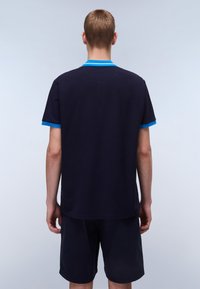 Marineblå polo skjorte med blå ribbede krage og ermeinnsatser, vist fra baksiden. Stoffet ser glatt ut med minimale teksturdetaljer.