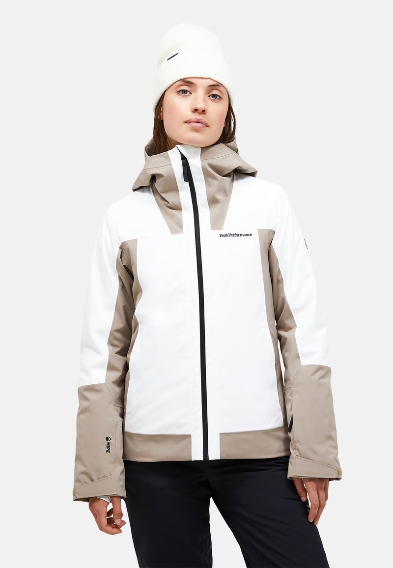 Weiß und hellbraun wasserabweisende Jacke mit Kapuze, ausgestattet mit einem schwarzen Reißverschluss, einem Logo auf der Brust und elastischen Bündchen. Sanfte Textur.