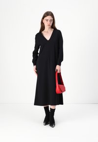 Musthave mustriga, millel on V-kaelus, on valmistatud siledast kangast. Kombineeritud punase käekotiga ja mustade teravate varbaotsaga ankle boots'idega.