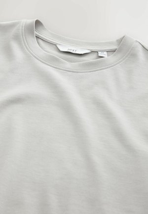 Tricou gri deschis cu guler rotund, fabricat dintr-un material de bumbac moale. Are mâneci scurte și detalii cusute pe guler și tiv.