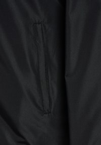 Tejido de chaqueta negra que presenta un bolsillo con cremallera en la costura lateral. El material tiene una textura suave y mate sin patrones o acentos visibles.