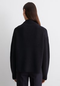 Schwarzer Strickpullover mit hohem Kragen, gerippter Textur, überschnittenen Schultern und lässiger Passform. Rückansicht, keine sichtbaren Verzierungen.