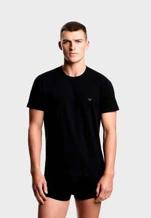 Black cotton t-shirt with short sleeves, round neckline, and small logo on the chest. Model pair with black shorts, standing against a light background.