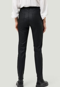 Jeans skinny noirs avec une texture lisse, poches arrière et un design ajusté. Portés avec des bottes noires à la cheville et un haut blanc.