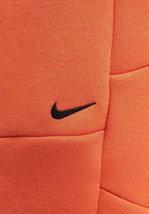 Tejido texturizado naranja con un logotipo de Nike negro bordado. Presenta un diseño suave y atlético adecuado para ropa deportiva.