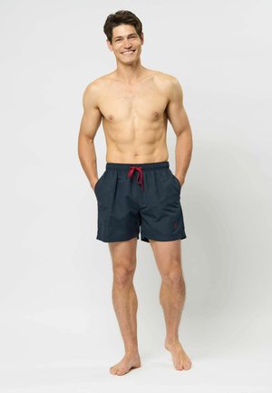 Shorts de bain bleu marine avec cordon rouge, taille élastique, poches latérales et détail de logo ; tissu léger et lisse.